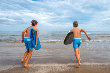 Two boys wearing swim suits at the beach running into the water together