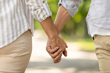 Unrecognizable mature man and woman holding hands while walking together in park