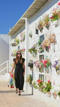 Woman dressed in black with a bouquet of red and white roses in her hand walks through a cemetery