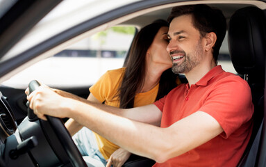 Fototapeta premium Loving young woman kissing her happy husband driving car