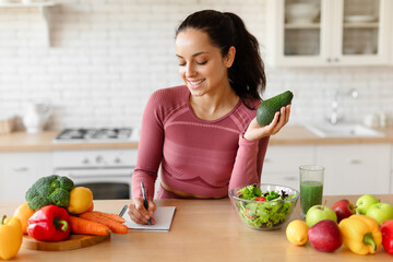 Fitness Woman Writing Down Healthy Recipes Holding Avocado At Kitchen