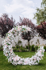 A beautiful wedding round arch, decorated with flowers, electric hanging lamps, stands on the green...