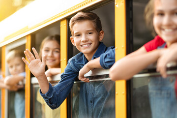 Group Of Pupils Peeking Out Of School Bus Window And Waving Hands
