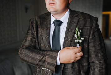 Stylish adult man holding, adjusting flower boutonniere on trendy brown suit jacket with black tie....