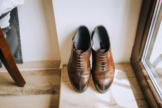 Men's brown leather stylish shoes stand near the window against the background of the wall. Close-up photography, business.