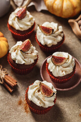 Pumpkin and cinnamon cupcakes with white cream decorated with figs on beige concrete background. Autumn festive dessert. Close up view, selective focus