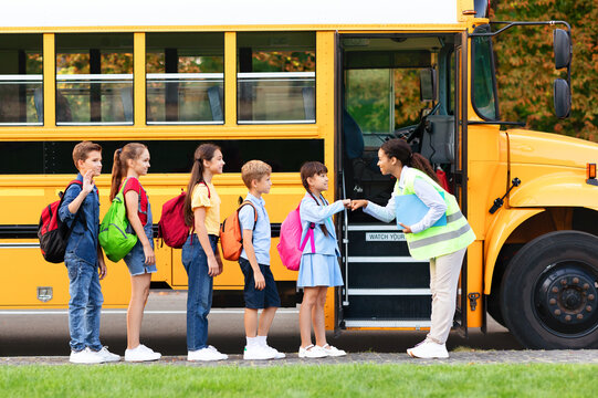 Black female teacher giving fist bumps to students near school bus