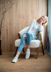 Woman sitting in armchair in living room laughing, enjoying free time