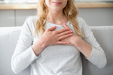 Calm woman holding hands on heart chest, feeling grateful