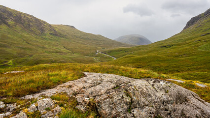 Fototapeta na wymiar Fog-covered green mountains and hiking trails in the Glencoe Valley, Scotland.