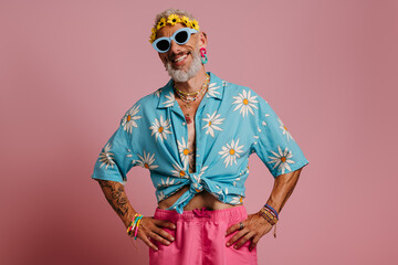 Bearded gay man in stylish shirt and floral wreath on head smiling against pink background