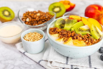 Bowl of granola with yogurt and fresh berries on a texture table. Yogurt berries, acai bowl, spirulina bowl. Healthy food, balanced breakfast. Strawberries, blueberries, kiwi, peach, almonds and chia.