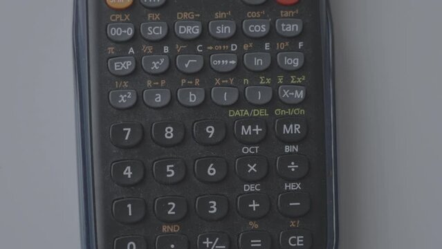 Small electronic device with keyboard and visual display for mathematical calculations. Dark calculator with dust lies on white table at home.