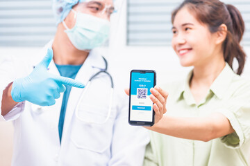 Asian young woman in medical mask show app smartphone mobile digital screen vaccinated coronavirus (COVID-19) certificate after getting vaccine prevent and doctor pointing to confirm certificate