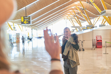 couple saying goodbye at airport. man waving goodbye to woman in foreground out of focus.