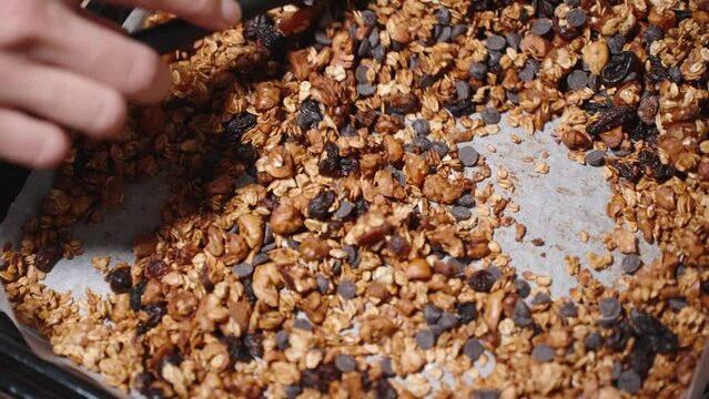 She stirs the freshly baked Granola with a spatula just out of the oven, top view. Slow motion.
