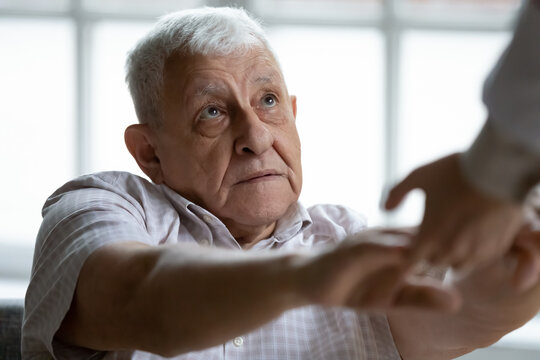 Close up of doctor or nurse hold hands help sick disabled mature 80s male patient in clinic or hospital, caregiver support ill weak senior 70s man in retirement house, elderly healthcare concept