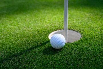 Closeup of white golf ball next to the cup on a putting green
