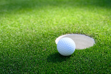 Closeup of white golf ball next to the cup on a putting green
