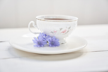 Obraz na płótnie Canvas Against the background of a mug with an invigorating drink. Cichorium flowers in a saucer. Flowers of ordinary chicory or cichorium dioecious. With space to copy. High quality photo