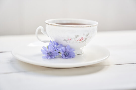 Against the background of a mug with an invigorating drink. Cichorium flowers in a saucer. Flowers of ordinary chicory or cichorium dioecious. With space to copy. High quality photo