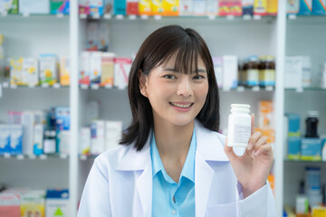 Young asian female pharmacist holding drug to camera with smiling at pharmacy counter. She holding drug with smiling at pharmacy shop.