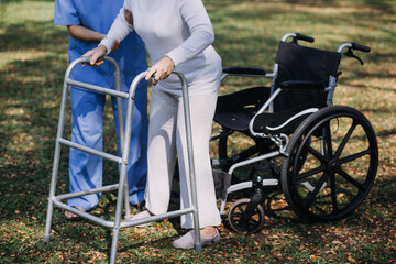 Fototapeta premium Asian young woman nurse at nursing home take care disabled senior man. Caregiver doctor serve physical therapy for older elderly patient to exercise and practice walking on walker or cane at backyard.