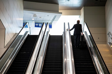  Three large escalators with a man in a business suit carrying a suitcase riding up on one of them.
