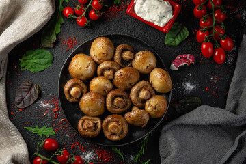 Grilled mushrooms in a dark plate on the table with spices, vegetables, herbs and onions.