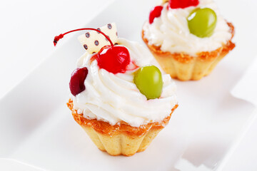 Beautiful cream cakes with cherries and grapes on a plate on a white background