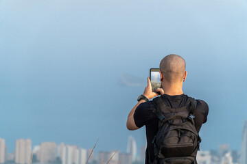 Young hiker with backpack recording a video with the smartphone to the landscape.