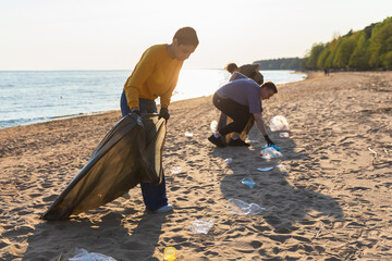 Earth day. Volunteers activists collects garbage cleaning of beach coastal zone. Woman and mans puts plastic trash in garbage bag on ocean shore. Environmental conservation coastal zone cleaning