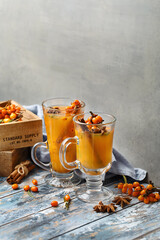 Two glass mugs with colorful hot sea buckthorn tea with cinnamon sticks, star anise and fresh sea...