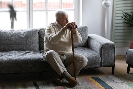 Upset old 80s disabled man sit on couch in retirement house lost in thoughts feeling lonely abandoned, lack communication, sad senior grandfather thinking or mourning at home, elderly solitude concept