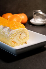 Delicious homemade mandarin cake roll with buttercream feeling, white plate and grey table background 