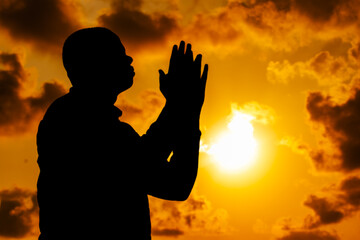 A captivating photograph showing the silhouette of a man. Pose of a humble and respectful man, as he says prayers in the impressive sunset of the solstice.