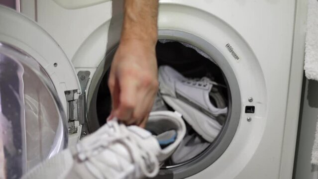 male hand takes white sneakers from laundry machine. Loading washing machine. Load clothes to washer machine. Load clothes laundry washing machine. Preparing laundry washing.