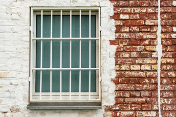 Fototapeta na wymiar barred window in an old brick wall painted white