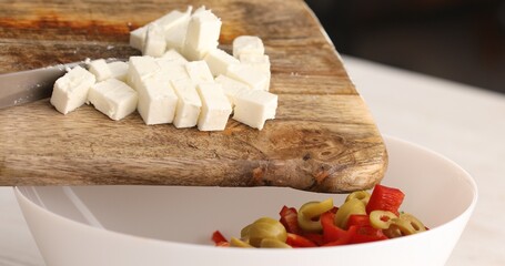 Sliced cheese is placed in a bowl with salad. Adding feta to vegetables. Preparing Greek salad. Healthy food.
