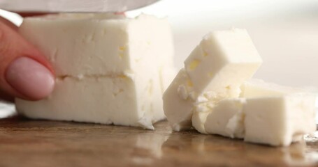 Close-up of Cutting or slicing cubes of feta cheese on a board for a Greek Salad. Healthy food.