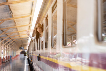 Young woman travelling by train and waving her hand out window