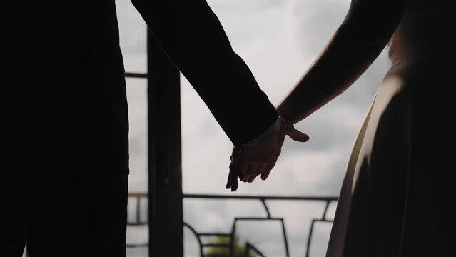 The silhouette of the lovers' hands against the background of light. A guy and a girl hold hands standing in front of the window