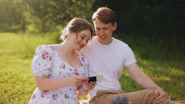 A girl and her boyfriend are looking at photos sitting on a blanket at a picnic. Close-up shooting