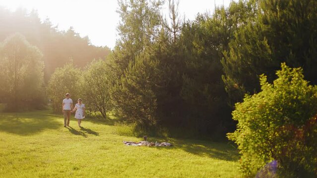 A guy and a girl are walking near their picnic spot. It's a cool sunny evening outside.