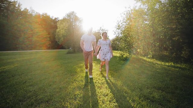 A couple in love runs against the background of the setting sun on the grass. The camera captures them in motion