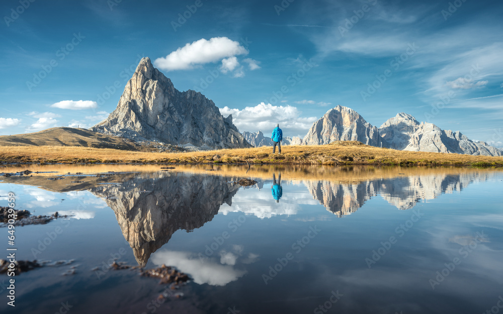 Wall mural man and mountains reflected in lake at sunset in autumn. passo giau, dolomites, italy. standing guy 