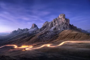 Keuken spatwand met foto Car light trails on mountain road and high rocks at night in autumn in Passo Giau, Dolomites, Italy. Landscape with blurred light trails, hills, mountain peaks, purple sky with stars in fall at sunset © den-belitsky