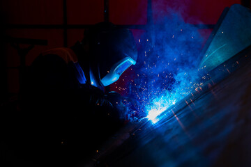 Skillful metal worker working with arc welding machine in factory while wearing safety equipment....