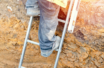 Builder going up the ladder to get out of trench © Iryna