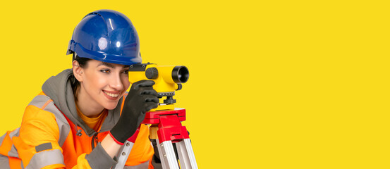 Woman in hard hat and yellow protective clothes land surveyor working with modern surveying...